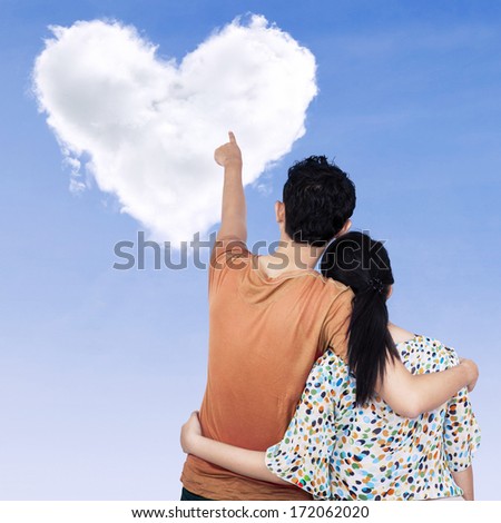 Young couple pointing at clouds shaped of heart on the sky
