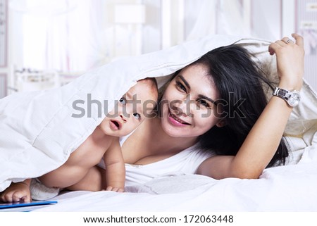 Happy young mother and her one year old daughter in bed at home