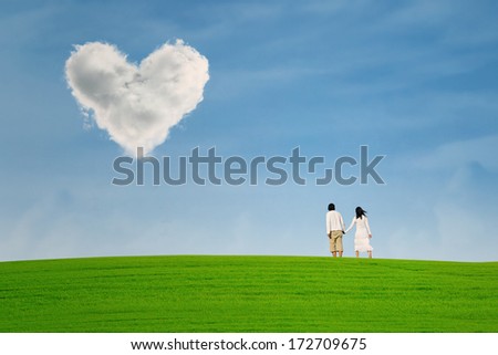 Couple at green field under heart shape cloud over the hill