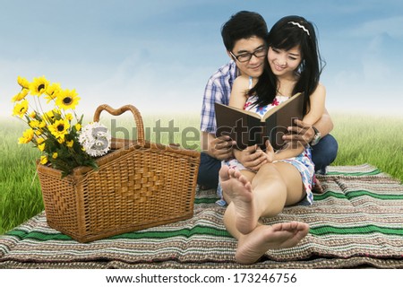 Boy and girl reading a book sitting on the grass in the park