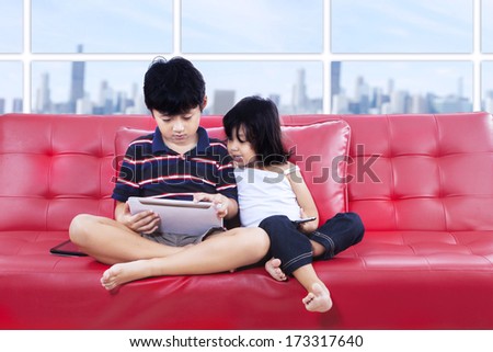 Children using tablet while sitting together on a red couch.