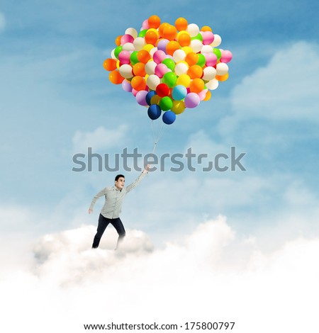 Young man flying with colorful balloons in blue sky
