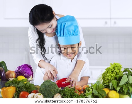 Asian mother is teaching her son to cut vegetable at home