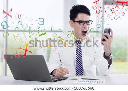 Angry young businessman looking at cell phone in office