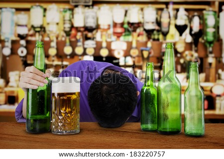 Drunk man sleeping in the bar, with bottle of beer in his hand