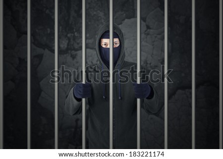 Behind bars. Arrested burglar in prison. Criminal with balaclava caught and arrested.