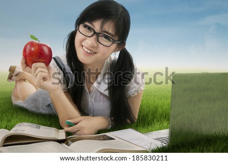 Female student holding a red apple while studying at the park