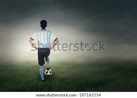 Back view of soccer player standing with a soccer ball at field