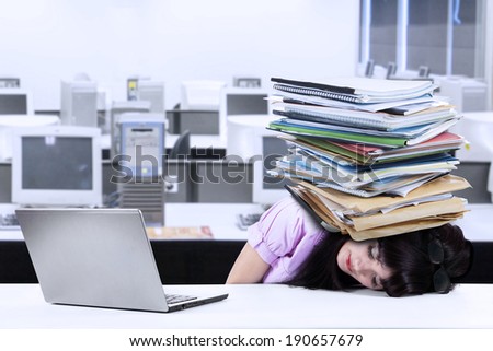Depressed young businesswoman with a pile of documents on her head at office
