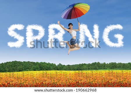 Happy woman with rainbow umbrella jumping in a colorful garden