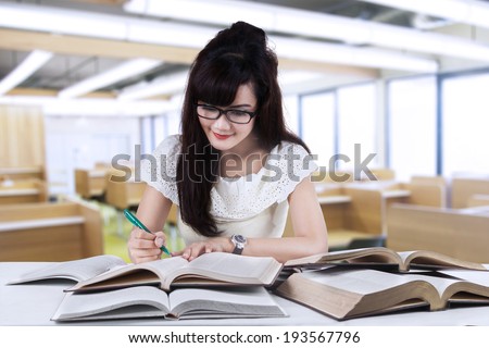Female student studying at reading room while writing the source on book