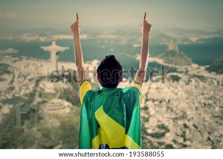 Backside of young man with a Brazilian flag on his back celebrating the competition time