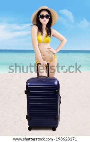 Beautiful asian woman with suitcase and swimsuit at the beach