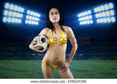 Sexy woman holding soccer ball at field. shoot at night