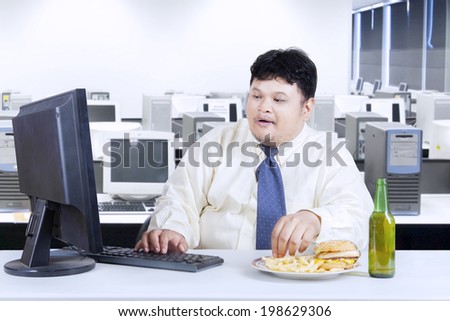 Obesity businessman working in office while eating junk food