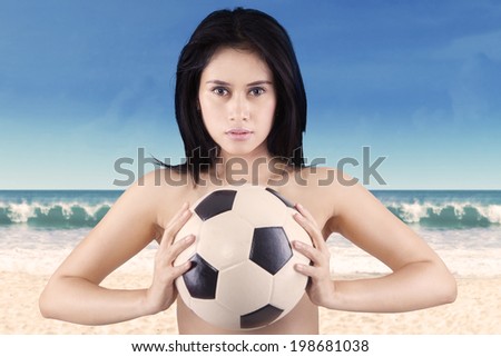 Young sexy woman holding a soccer ball on the beach
