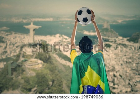 Backside of young man with a Brazilian flag on his back while holding a ball celebrate winning