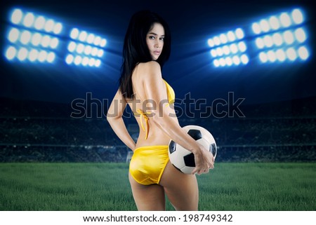 Beautiful woman in bikini holding a soccer ball. Shoot at soccer field