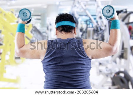 Fat man exercising with two dumbbells in the fitness center