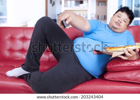 Overweight man eats pizza while watching tv at home