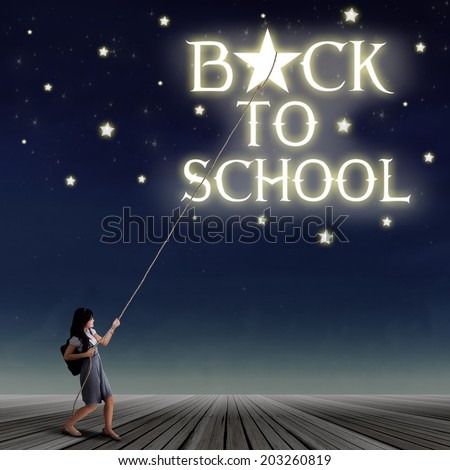 Portrait of young female student pulling down a back to school text and the stars with rope