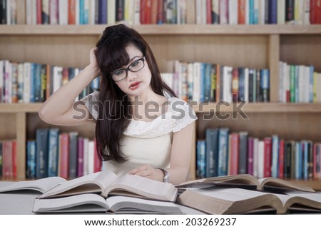 Confused female student reading many books for exam in the library