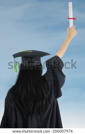 Woman in graduation gown rejoicing success. rear view