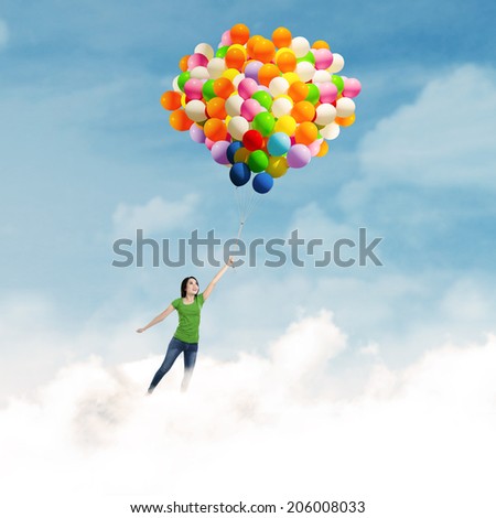 Happy young woman holding colorful balloons and flying over clouds