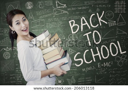 Female student studying at classroom while holding the source on book