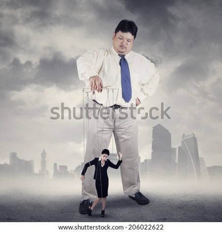 Businesswoman hanging on string and controlled by a businessman
