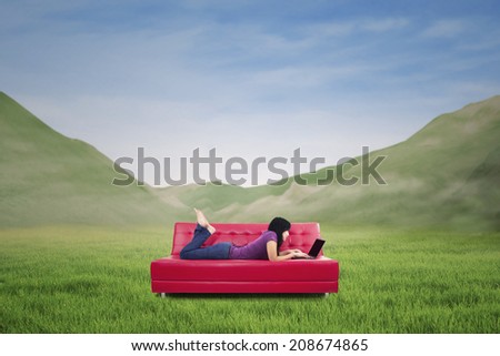 Young woman lying on couch with laptop - shot outdoor with mountain view