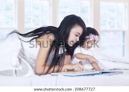 Close-up of a mother and baby girl reading book story on bed