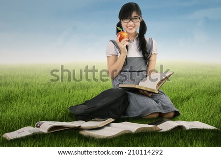 Female student holding a red apple while studying outdoors