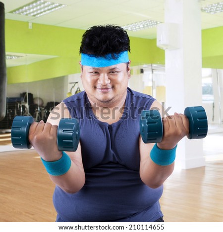 Fat man exercise in fitness center by lifting two dumbbells