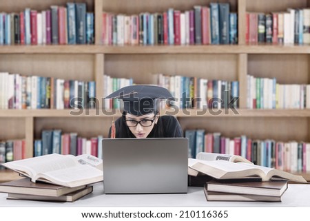 Young female graduate studying with laptop and books in library