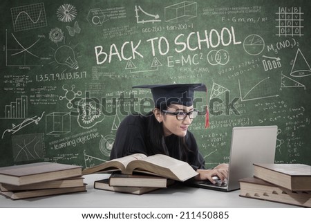 Young female bachelor studying with laptop and books in class