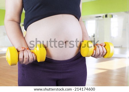 Pregnant female do exercise in a gym, front view, body part, lifting dumbbells