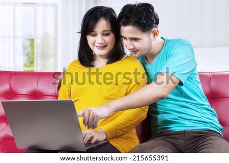 Portrait of asian man with wife pregnant using laptop on couch