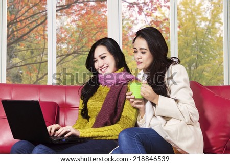 Two young asian girl using laptop together at home with autumn background on the window