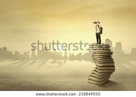 Little boy standing on books and use a telescope for looking his vision in 2015