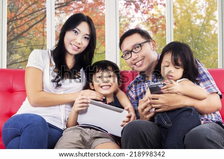 Young asian family smiling at camera while using digital tablet at home with autumn background on the window