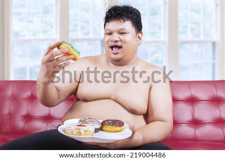 Cheerful fat man looking at donuts while sitting on the sofa at home