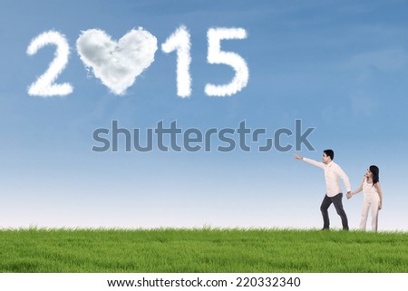 Young asian couple walking on the meadow and pointing at cloud shaped number 2015