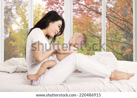 Happy mother sitting on bed while playing with her little daughter at home in autumn