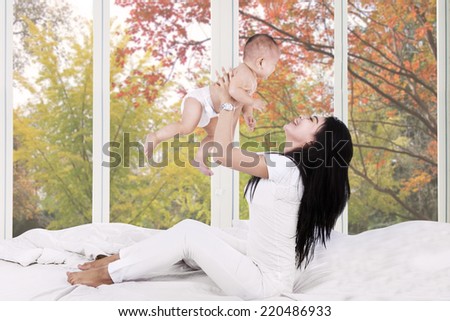 Young mother playing on bed with her baby at home in autumn