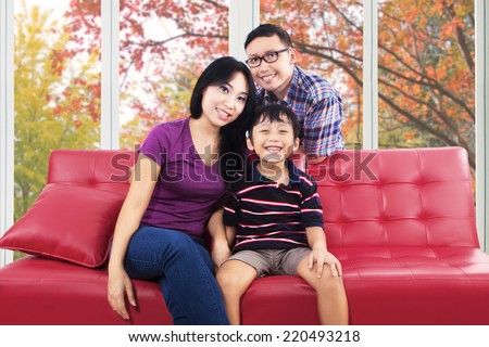 Happy asian family smiling at camera while sitting on sofa at home in autumn