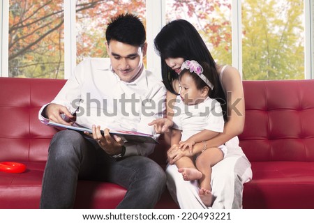 Hispanic family reading a story book on sofa at home in autumn