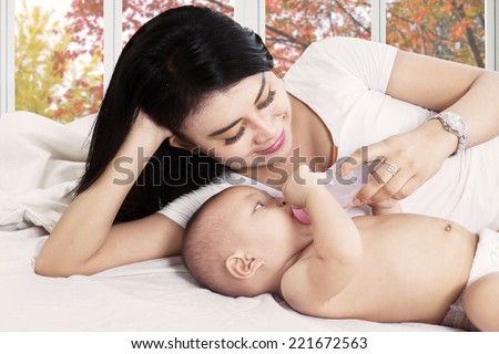 Asian mother feeding her baby girl on bedroom with a milk bottle