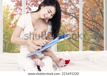 Cute baby read a story book with mother on bedroom