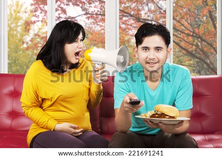 Hispanic pregnant woman feeling annoyed to her husband and yelling with a megaphone
